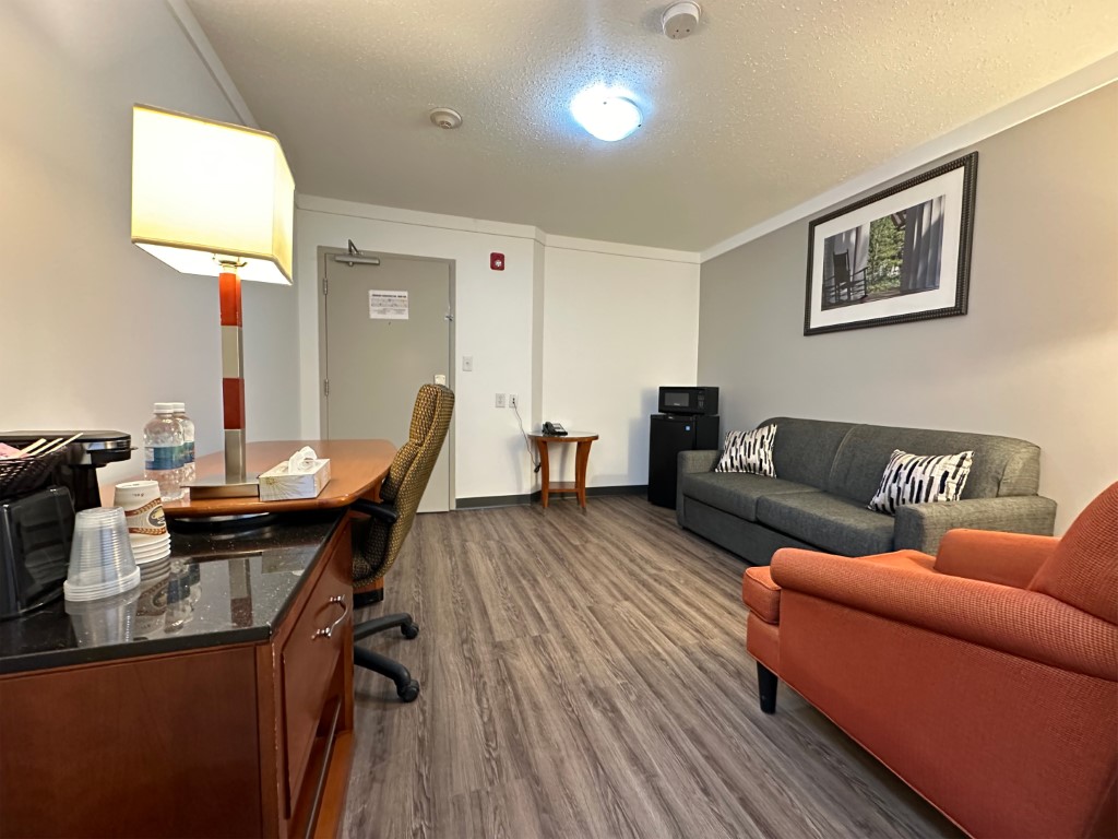 Suite living area with sofa, armchair, work desk, and microwave at Sunset Inn and Suites Sioux Lookout
