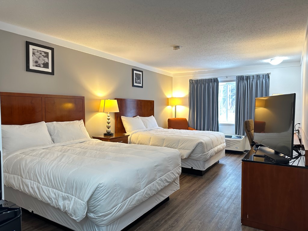 Double queen guest room with two beds, lamps, and a window at Sunset Inn and Suites Sioux Lookout